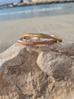 Bracciali Anima Tiziana Piola in bronzo dorato e oro rosa su una roccia in spiaggia