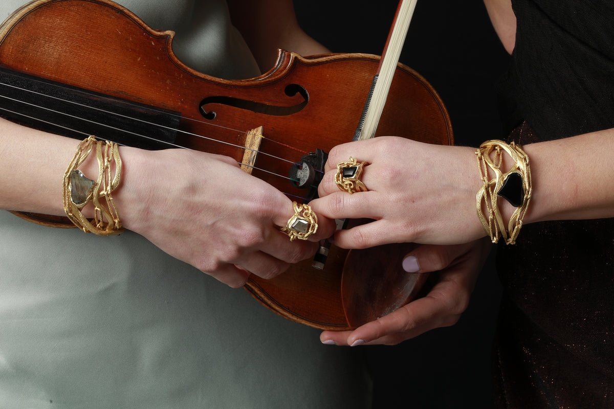 Mani che tengono un violino, con bracciali e anelli Tiziana Piola con pietre naturali