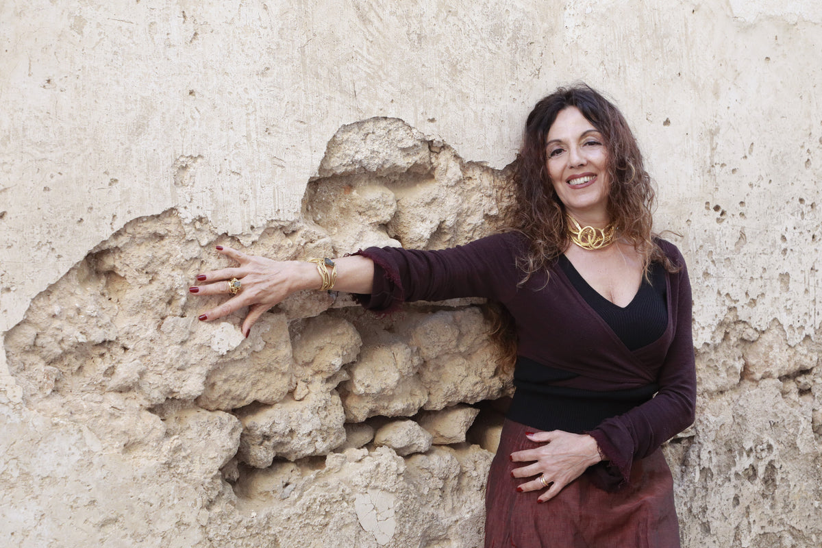 Donna davanti a un muro in pietra con collana e bracciale Tiziana Piola in bronzo dorato