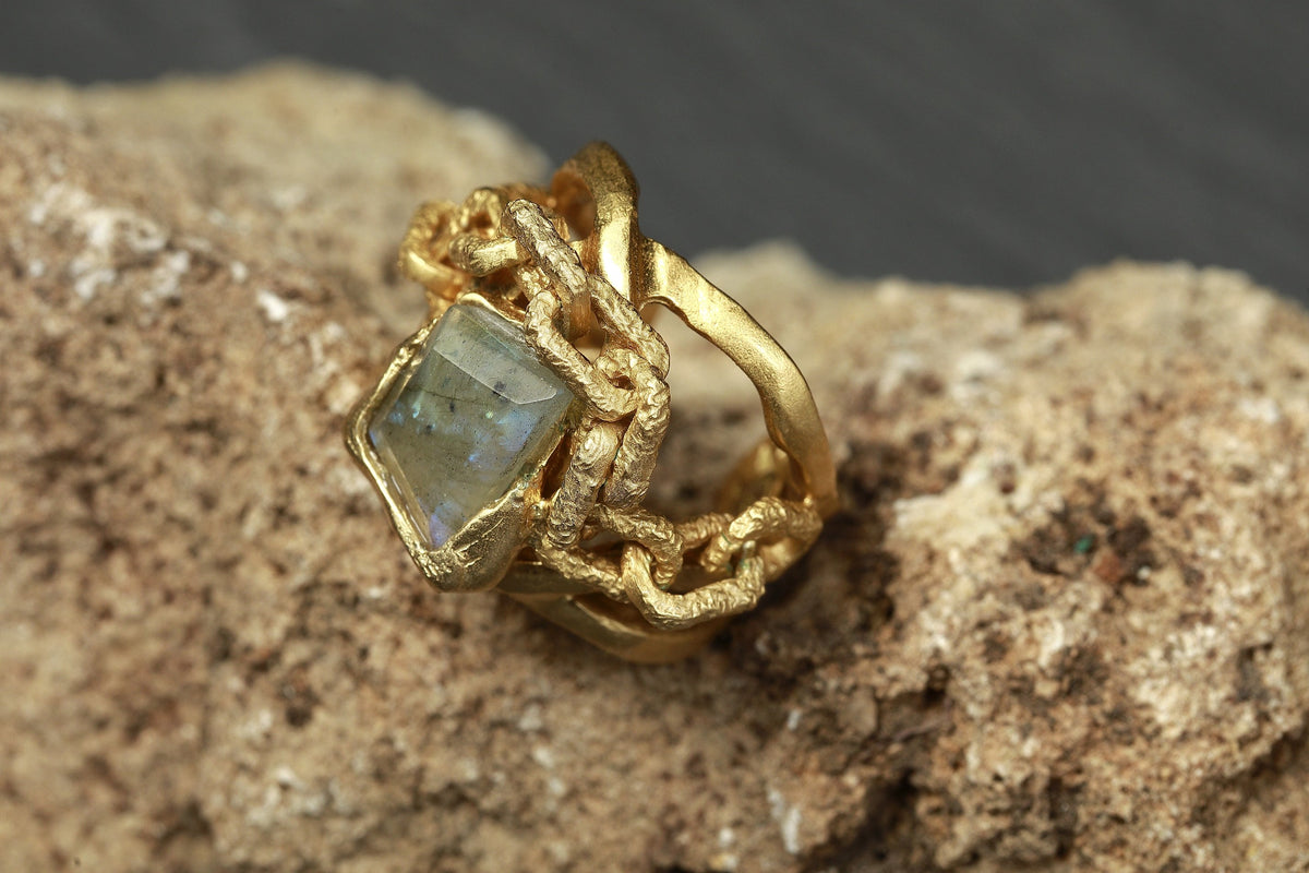 Anello Tiziana Piola in bronzo con bagno in oro 24 carati e pietra incastonata, appoggiato su pietra grezza